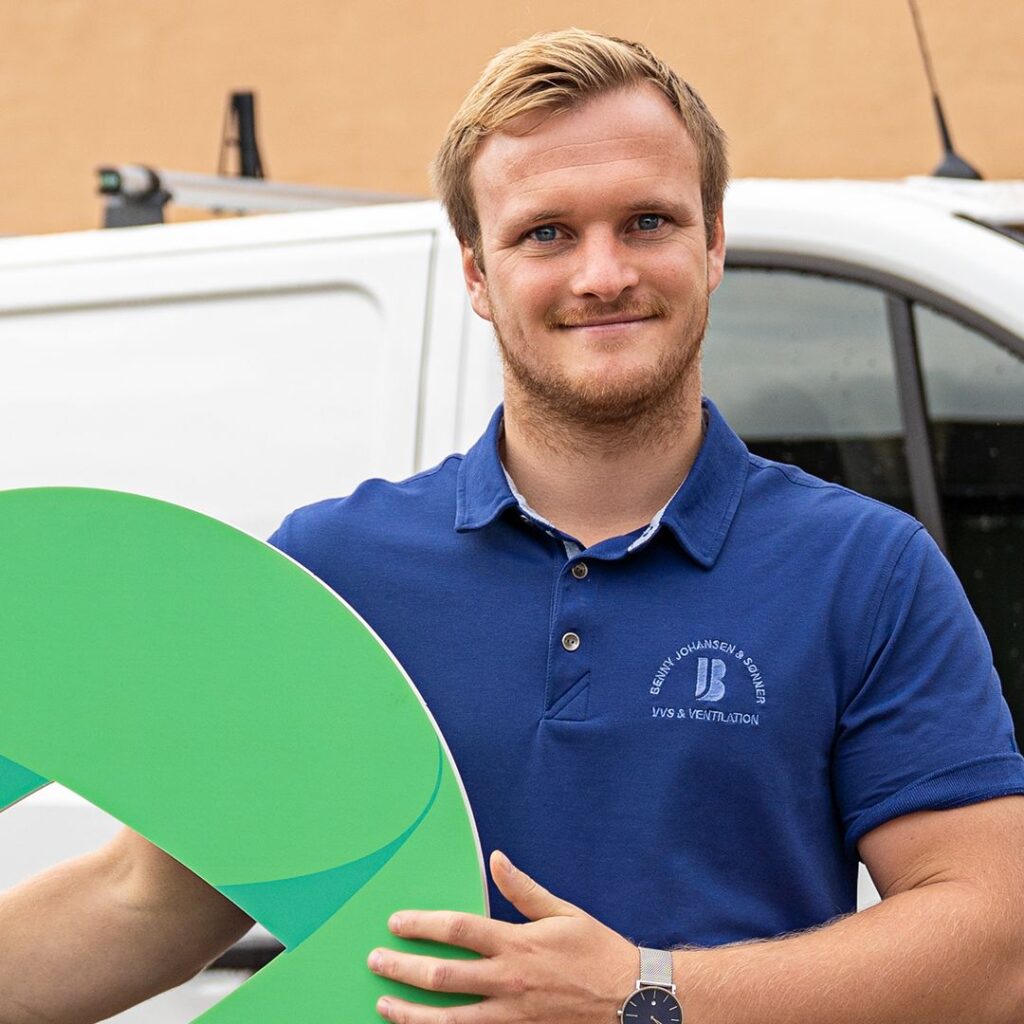Jonas Johansen der står og smiler til kameraet i en blå t-shirt mens han holder et stort Ordrestyrings logo