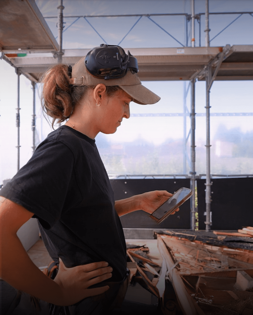 Kvindelig håndværker der står på en byggeplads og kigger på Ordrestyrings appen på sin mobil.